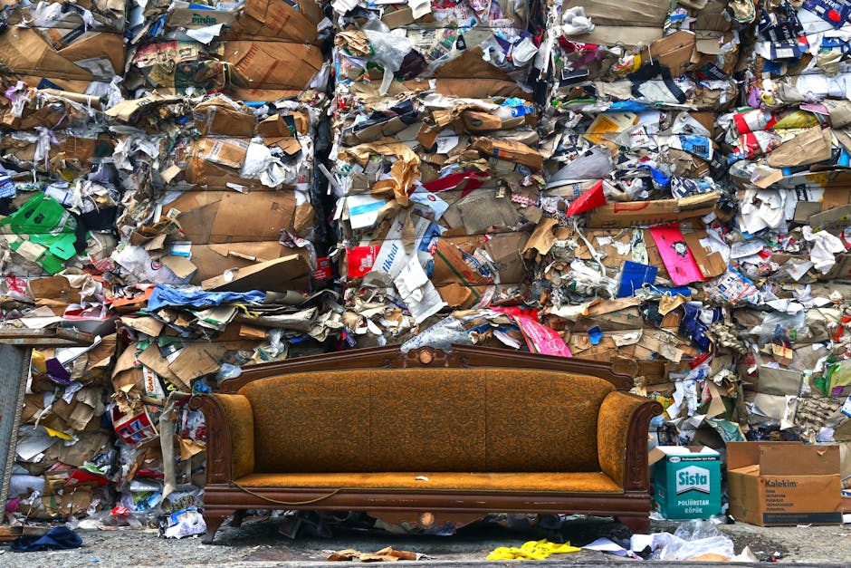 A black-and-white photograph showing an outdoor scene in a residential area where household waste and large furniture items have been discarded on a paved pavement. Visible objects include wooden gard